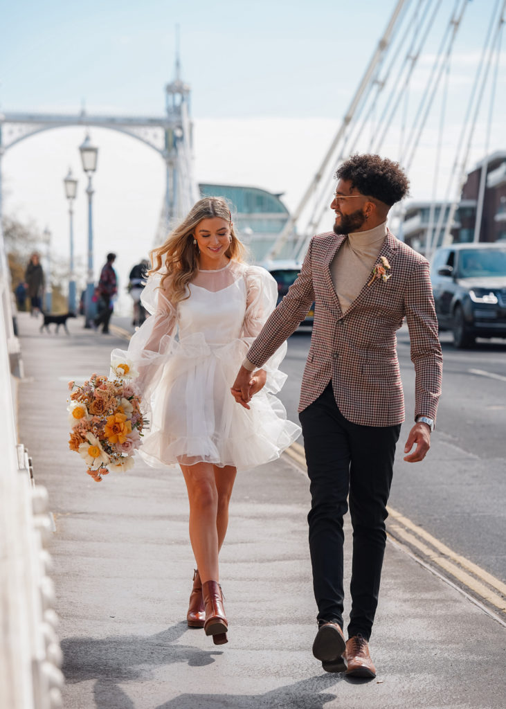 newly married couple walk across Chelsea bridge after london wedding