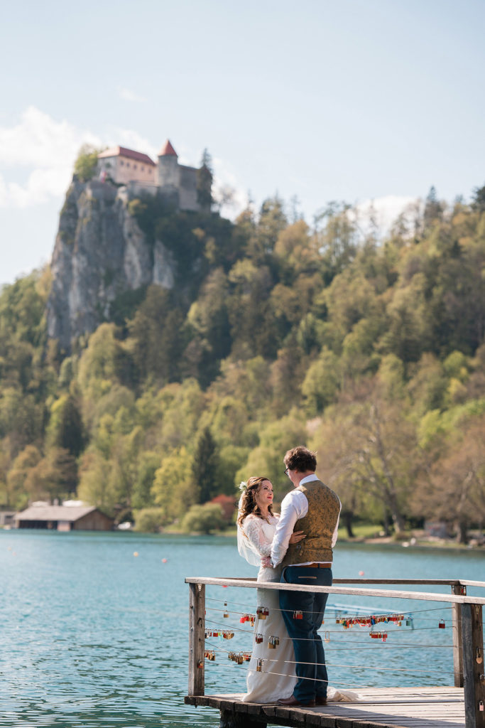 newly wed couple embrace on lake bled jetty after wedding