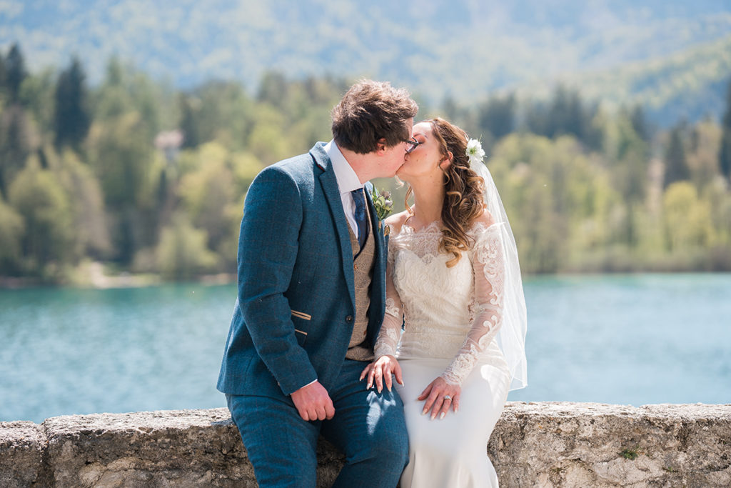 Bride and Groom sat on wall overlooking lake bled, kissing