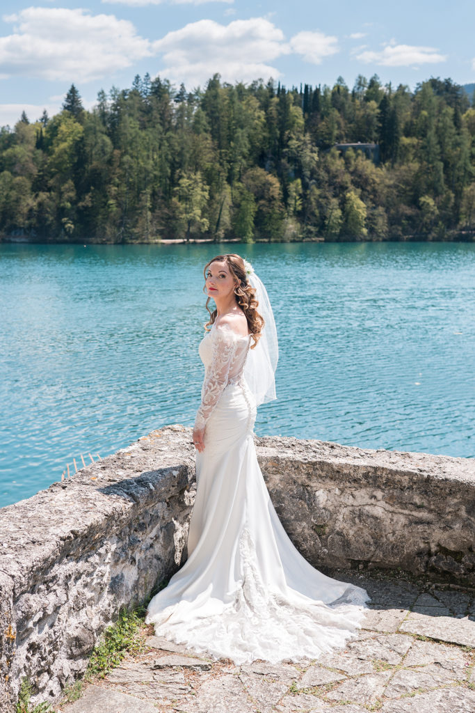 Bride stood at wall overlooking lake and mountains in Slovenia