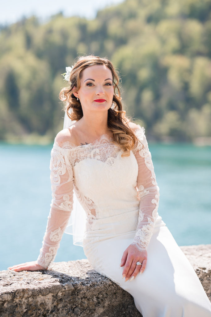 Bride sat on wall overlooking lake and mountains in Slovenia