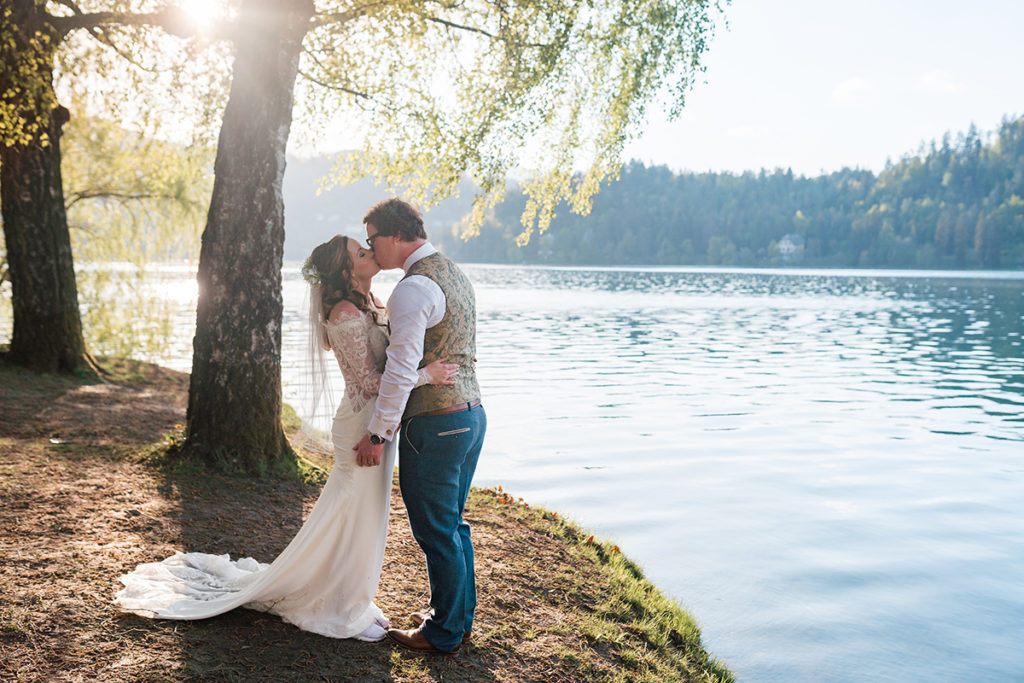 Bride and Groom kiss on edge of lake bled at sunset