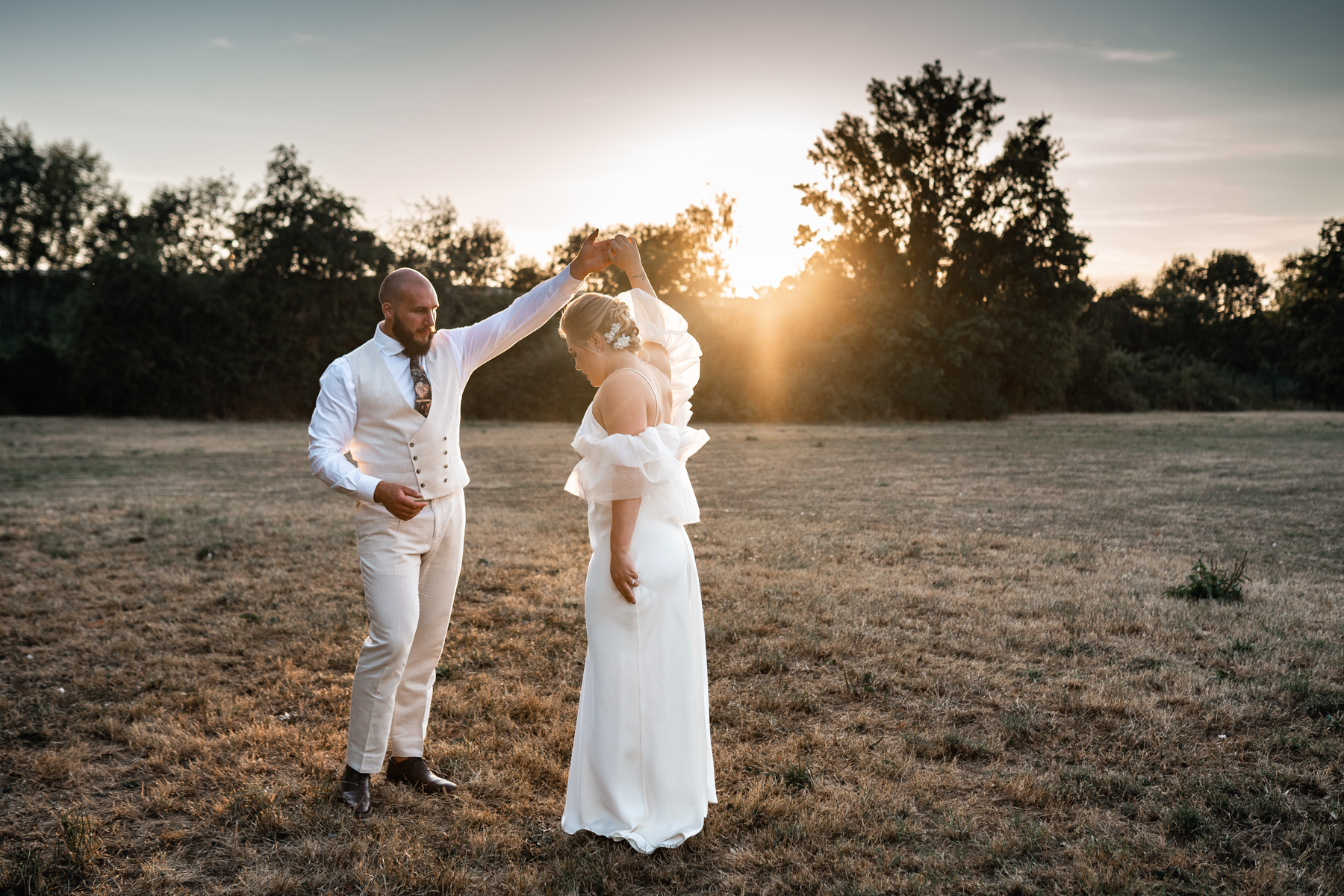 bride and groom dance with sunflares behind them