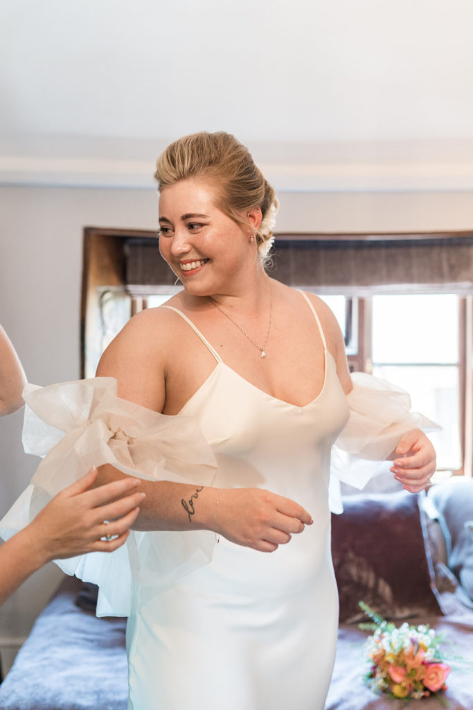 bride looks over shoulder at mum whilst putting on wedding gown