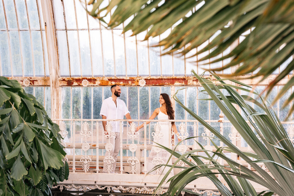 Couple wearing white hold hands in KEW gardens palm house at their engagement photoshoot 
