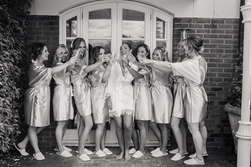 black and white photo of bride and bridesmaids cheering with champagne at Chewton Glen