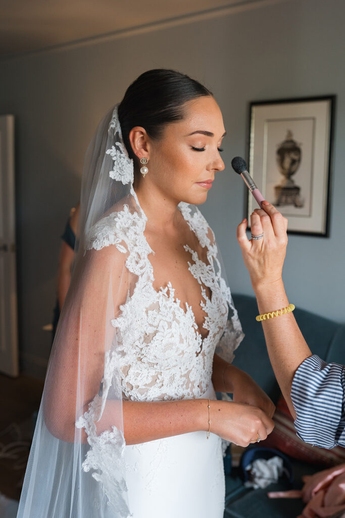 make up artist holds brush by brides face as she completes finishing touches before the wedding 
