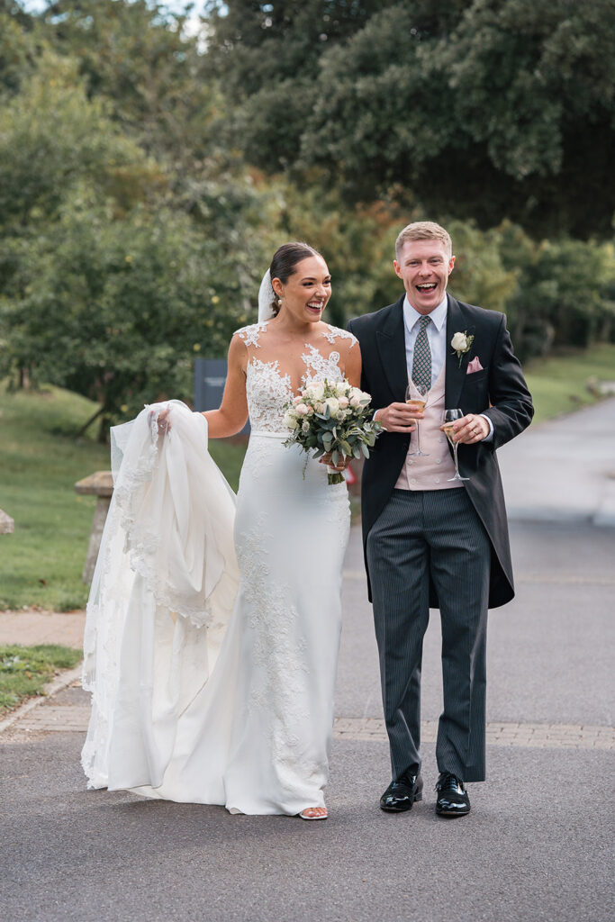 Bride and groom laugh, holding champagne after Chewton Glen wedding ceremony