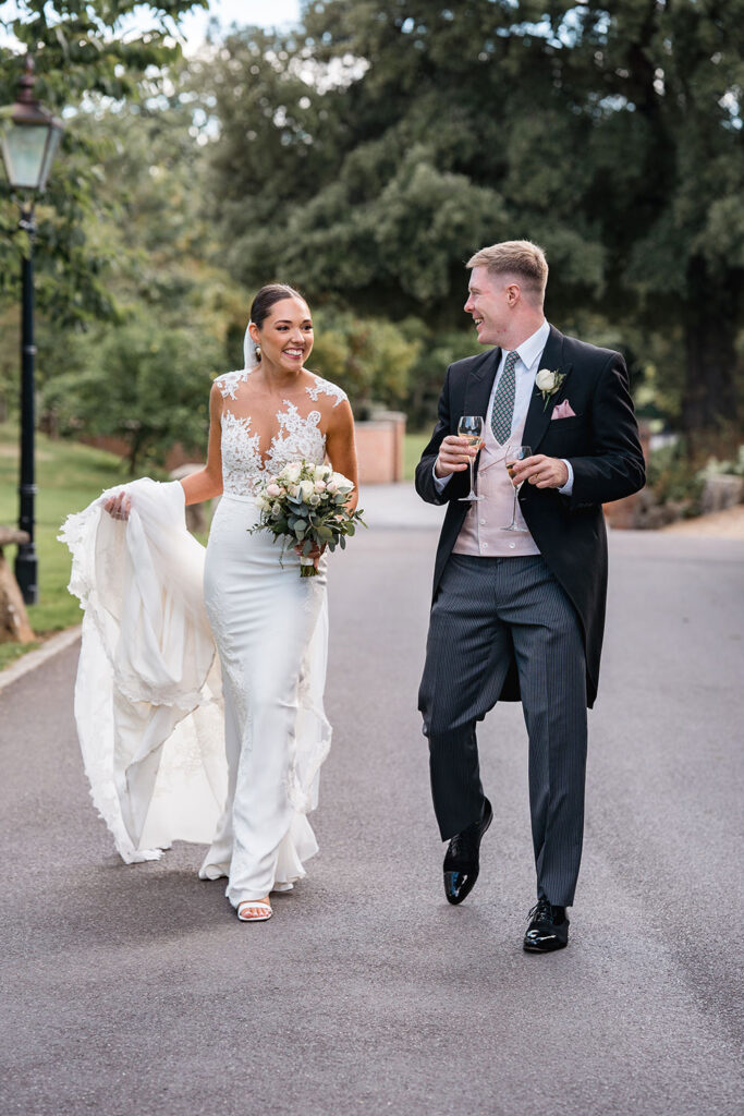 Bride and groom laugh, holding champagne after Chewton Glen wedding ceremony