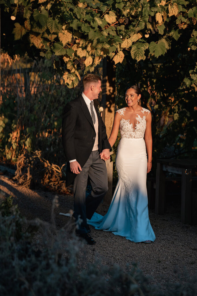 Bride and groom walk through gardens at Sunset at Chewton Glen Wedding