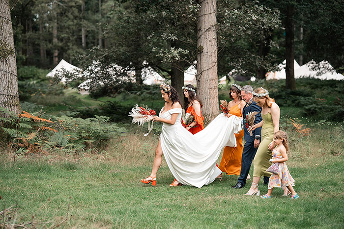bride walking through Harewood Forest, with bridesmaids carrying her train