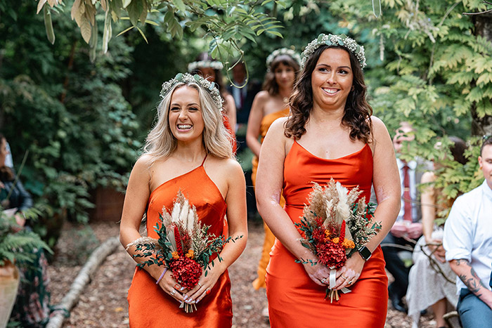 Bridesmaids smiling as they walk down the aisle in Orange silk dress