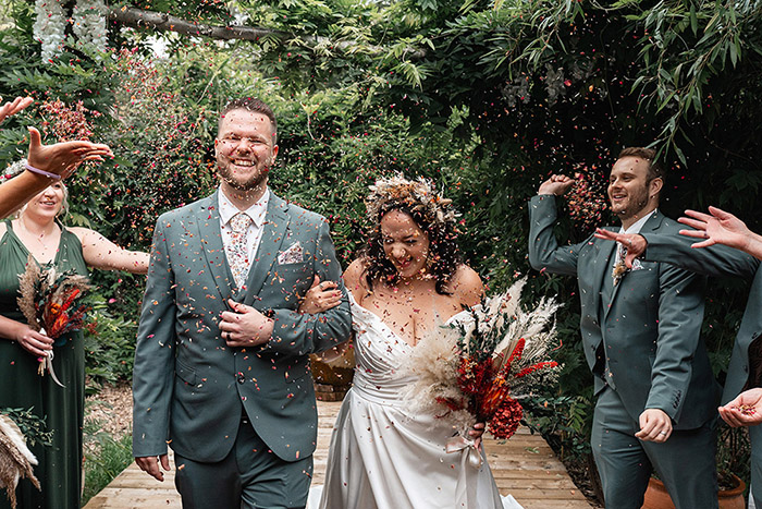 bride and groom walking down aisle at Harewood Forest Wedding, they are grinning, surrounded by dried confetti