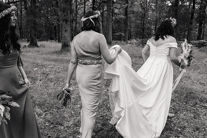 black and white image of a bridesmaid carrying brides train through the forest