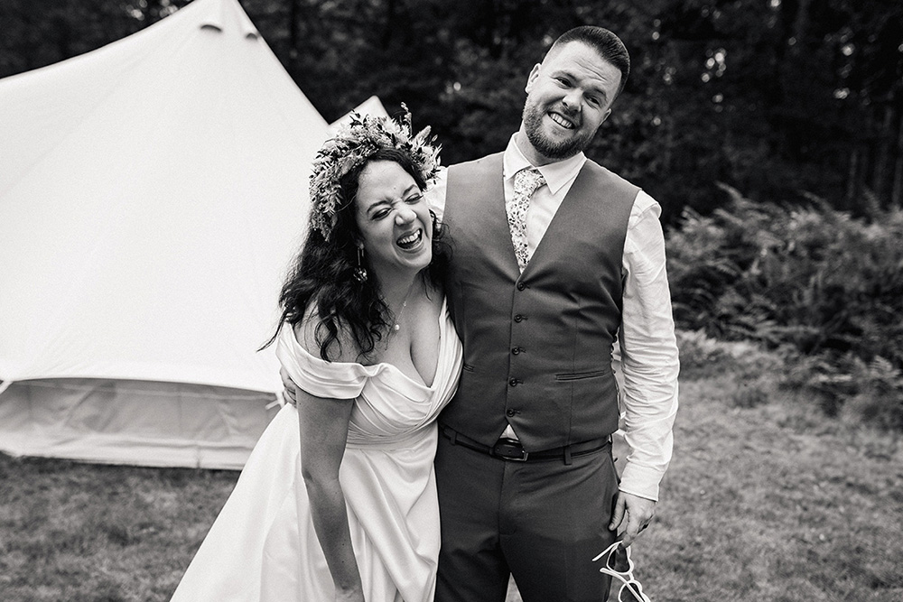 bride and groom stood outside a teepee, wearing love heart glasses in black and white