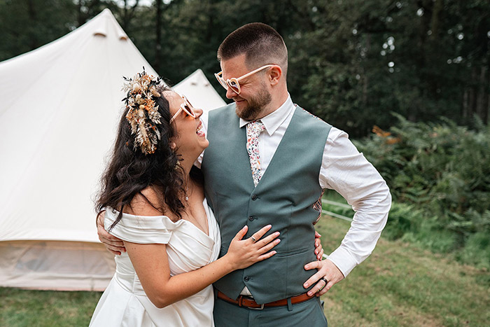 bride and groom stood outside a teepee, wearing love heart glasses at DIY wedding
