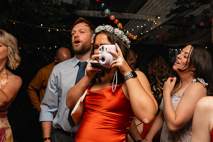 guest in orange dress uses polaroid on the dancefloor to take photo of another guest