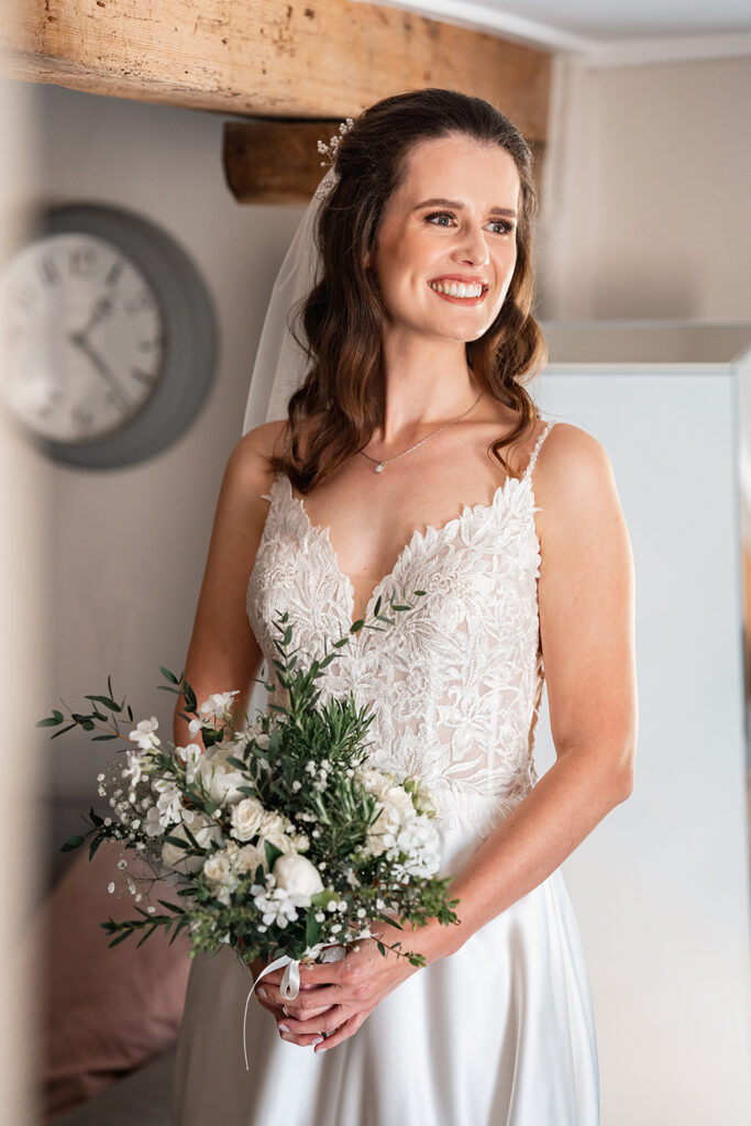 Bride smiles out of the window at Sopley Mill, wearing lace wedding dress and holding a white bouquet