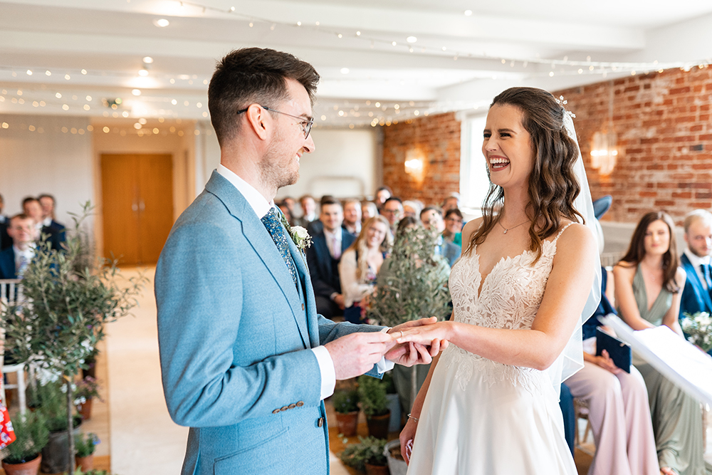 groom places ring onto brides finger at sopley mill wedding, both laugh