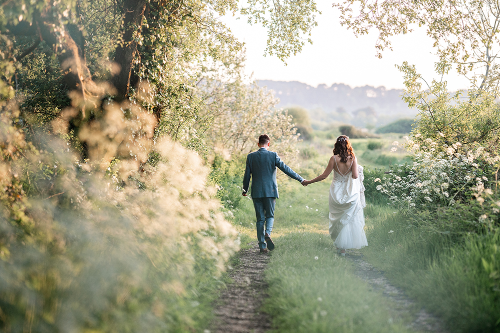 bride and groom smiling at camera, embracing each other in wild flower meadow at sopley mill