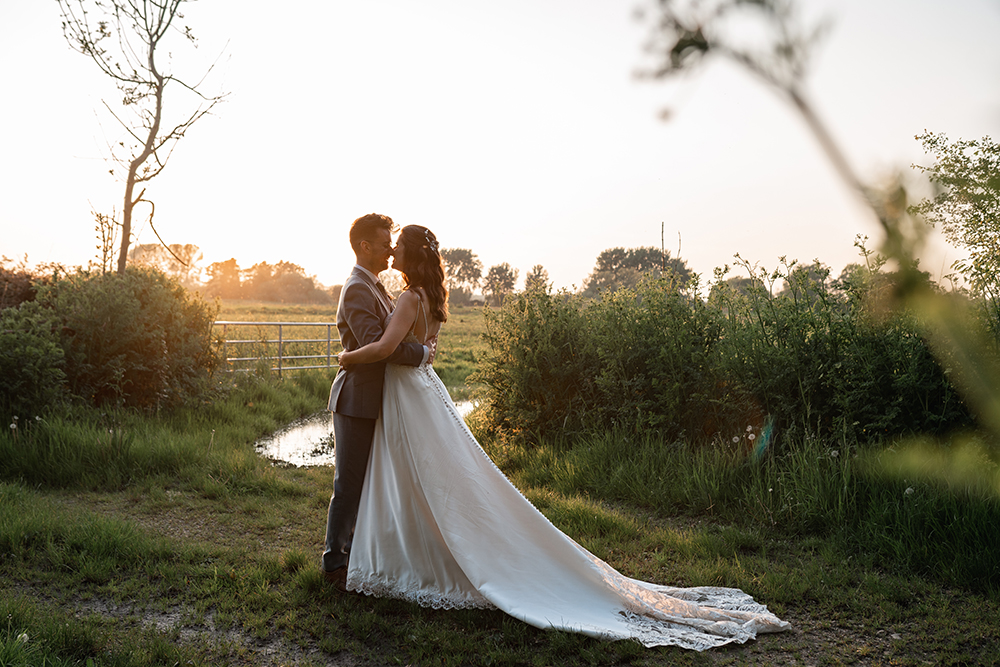 couple embrace, with brides train fanned out behind her, overlooking the river at sopley mill