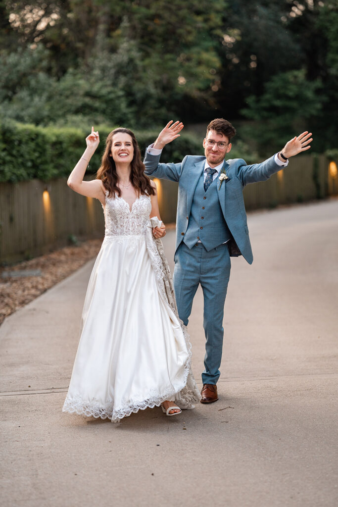 couple wave hands in the air outside Sopley mill during their wedding photos