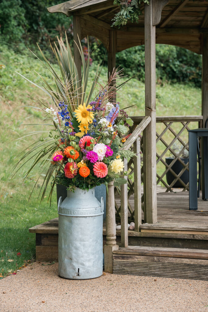Floral display in milk churn at outdoor wedding