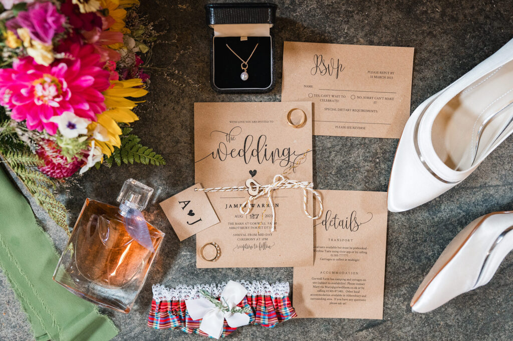 Flatlay of DIY wedding invites, shoes, perfume and flowers in rustic barn wedding style