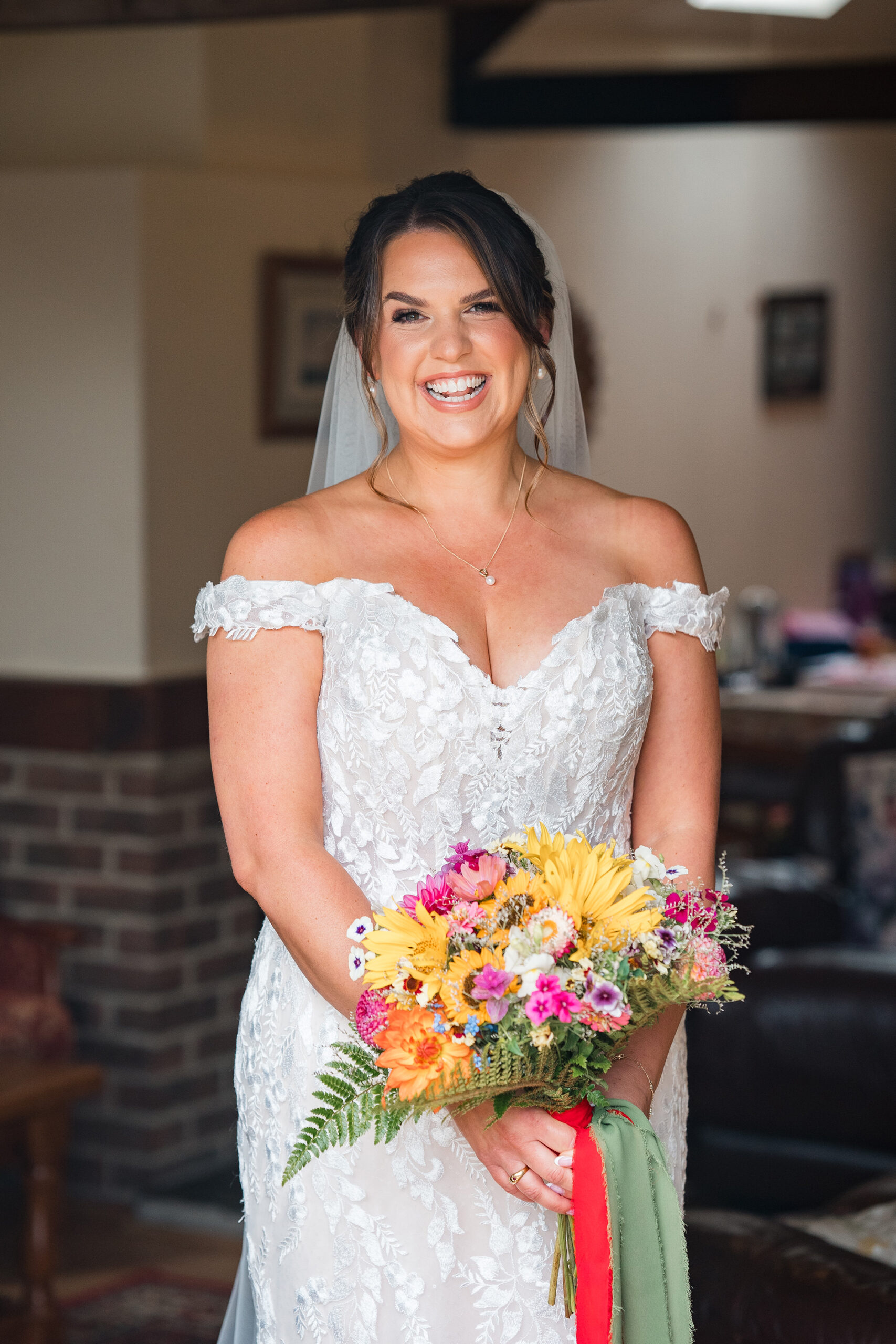 Bride smiling in lace dress with colourful bouquet on wedding day