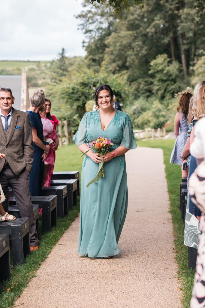 Bridesmaid in green dress smiles whilst walking down aisle at Gorwell Farm Weding