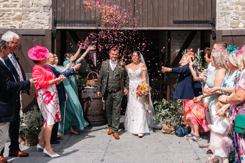 bride and groom are showered in pink confetti as they leave Gorwell Barn