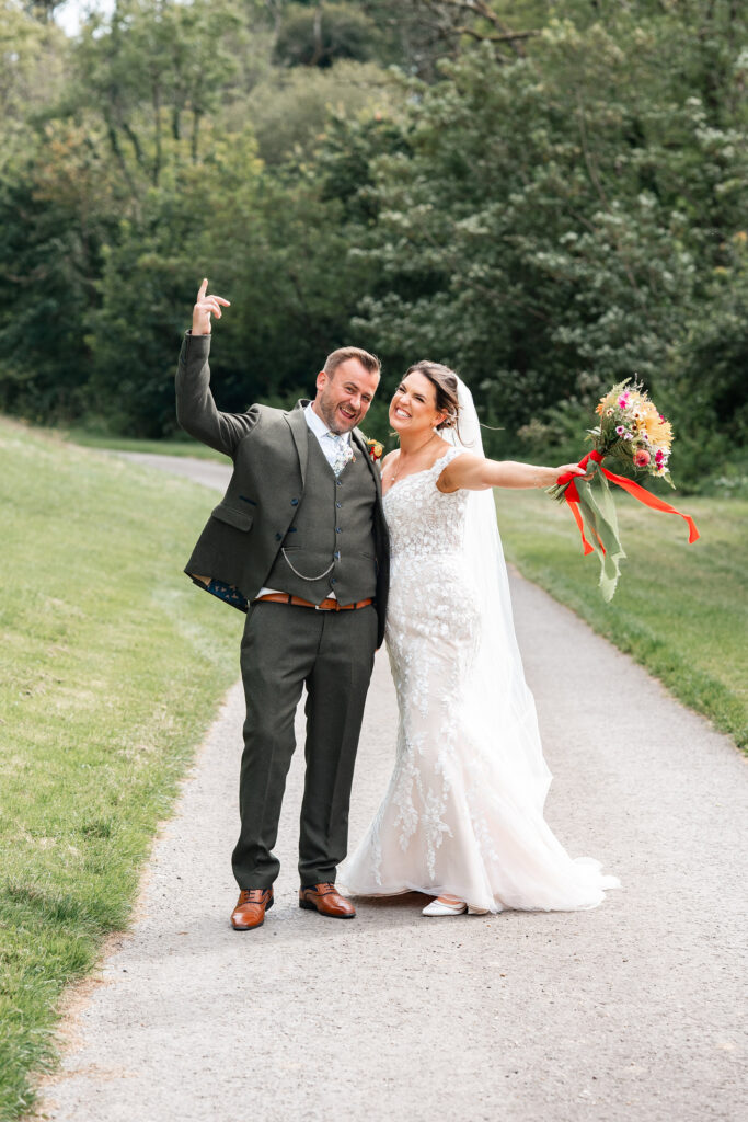 bride and groom wave hands in the air during couple portraits at Gorwell Farm wedding