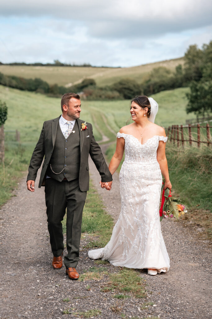 bride and groom walk and smile at eachother in hilly landscape in the Purbecks