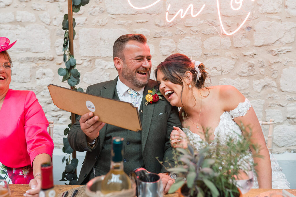 bride and groom lean on each other, laughing during wedding day speeches