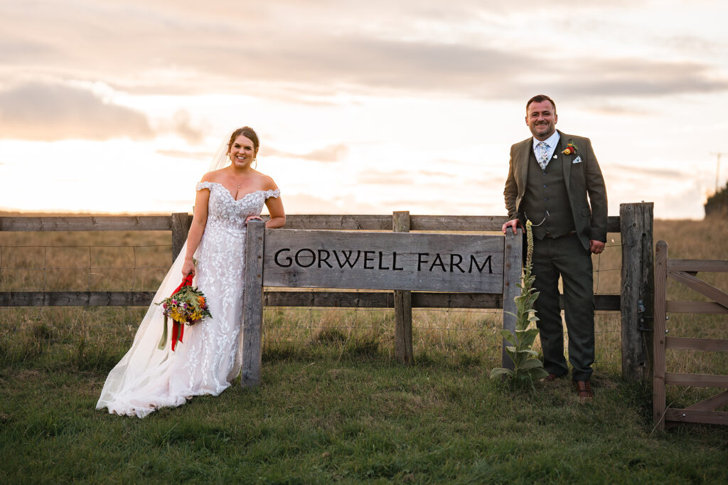bride and groom stand hand in hand at sunset overlooking gorwell farm wedding venue