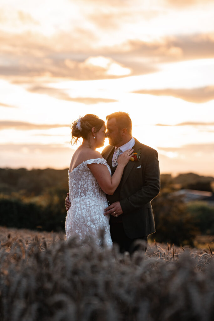 Bride and Groom embrace in wheat field at sunset on wedding day at Gorwell Farm