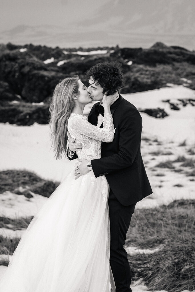 couple kiss on snowy plains of iceland. Woman wears Mara Marie wedding dress and the Man a black suit