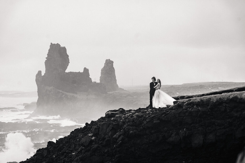 Young couple in wedding atire stand on cliff edge in Iceland