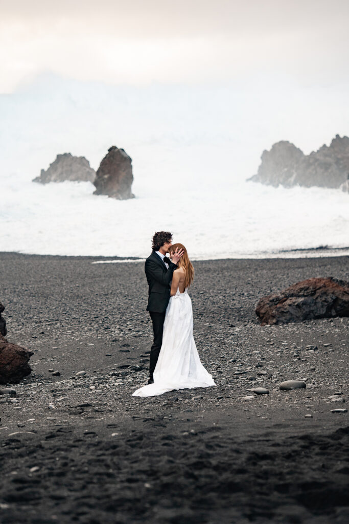 bride and groom embrace on black sand beach, iceland