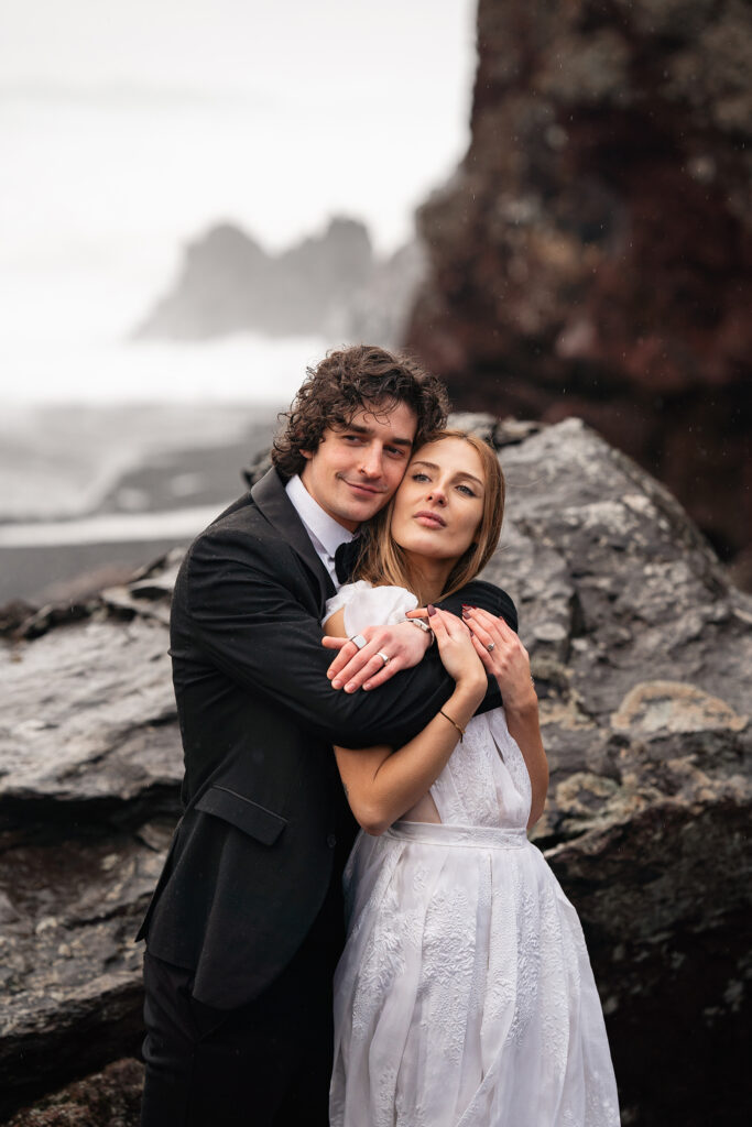 bride and groom embrace on black sand beach, iceland