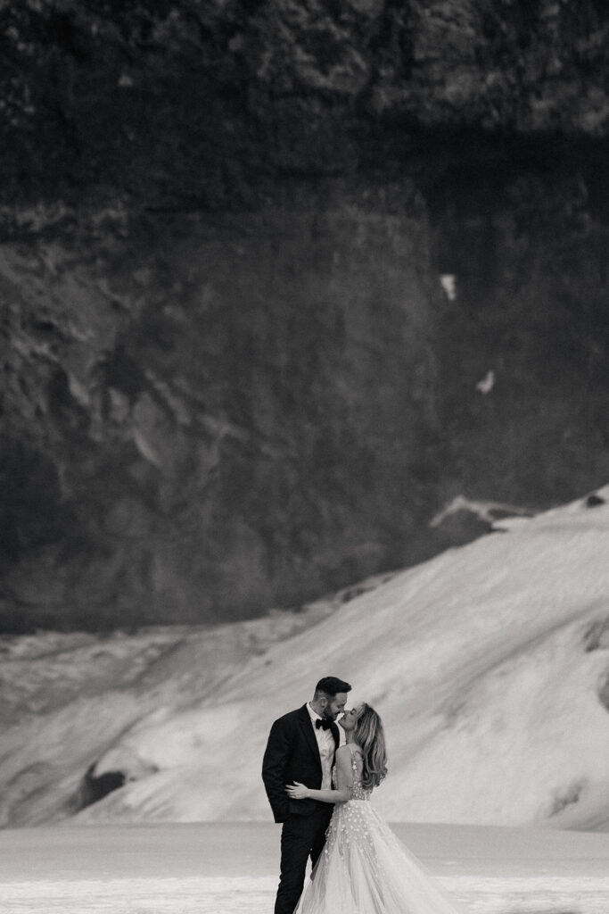 black and white image bride and groom kiss in front of Seljalandsfoss, Iceland waterfall