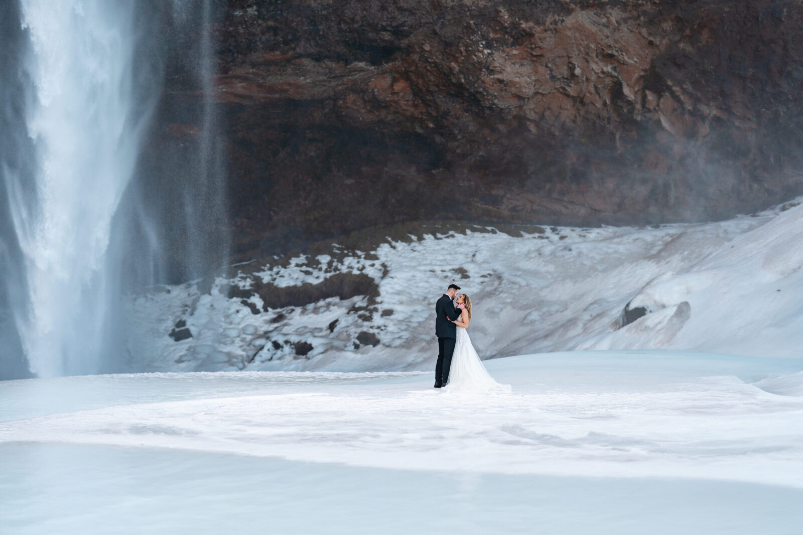 bride and groom kiss in front of Seljalandsfoss, Iceland waterfall