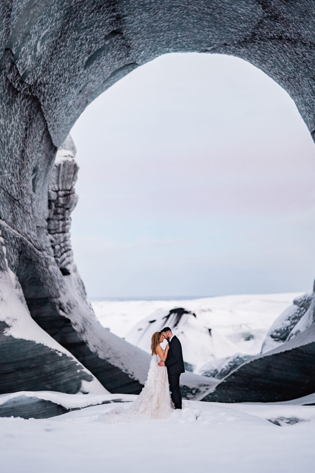 bride and groom stand in front of ice cave at Icelands famous glacier for wedding