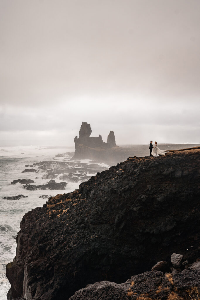 bride and groom in Iceland stand on rugged cliff overlooking ocean