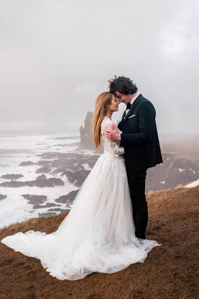 bride and groom in Iceland stand on rugged cliff overlooking ocean