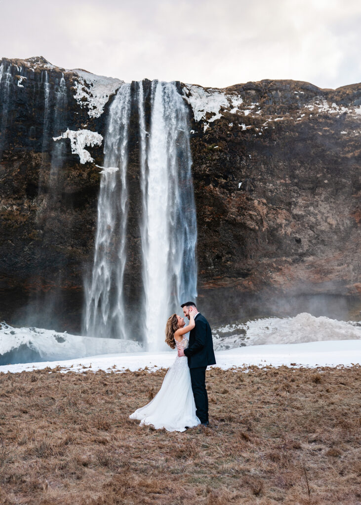 newly married couple embrace in front of Seljalandsfoss, Iceland waterfall at Iceland Elopement