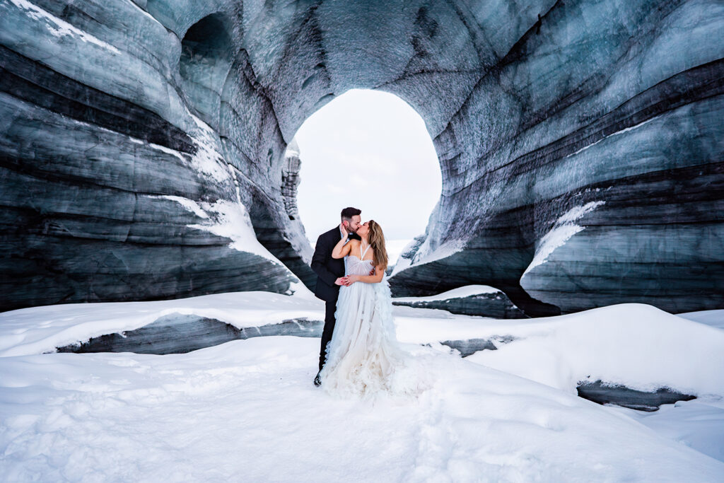 bride and groom stand in front of ice cave at Icelands famous glacier for wedding