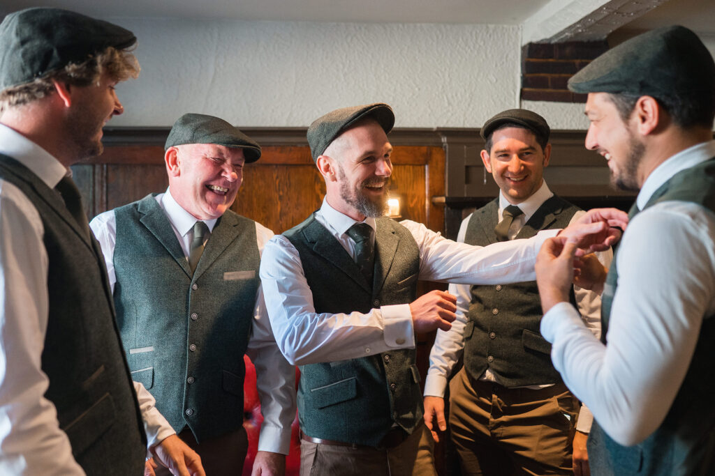 groom and his groomsmen laugh together trying to do their ties up