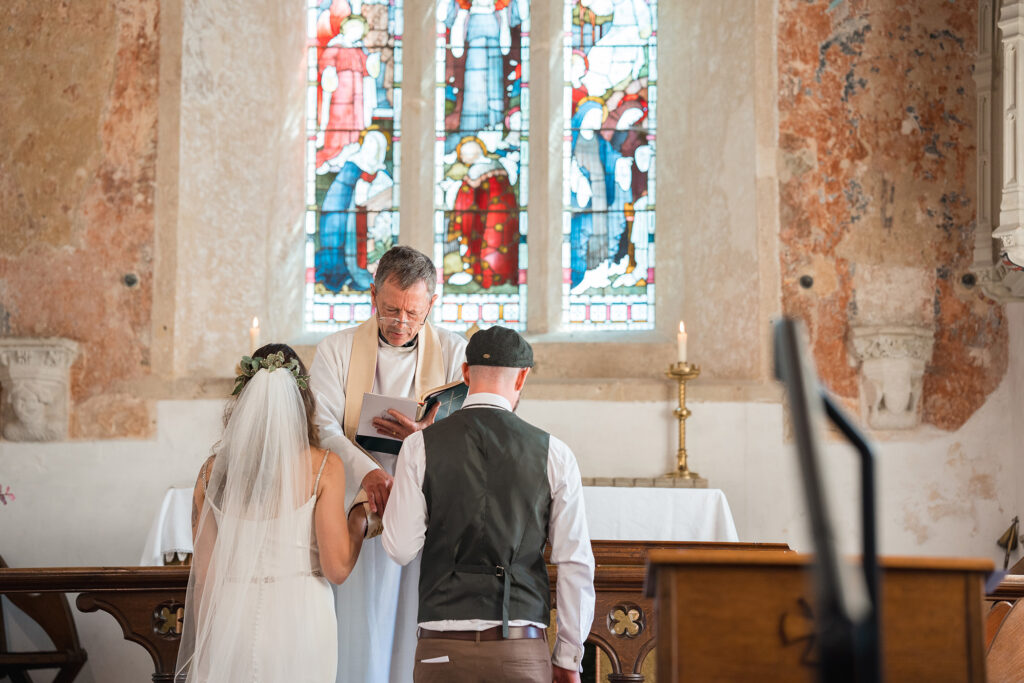 bride and groom in prayer beneath stain glass window at new forest wedding