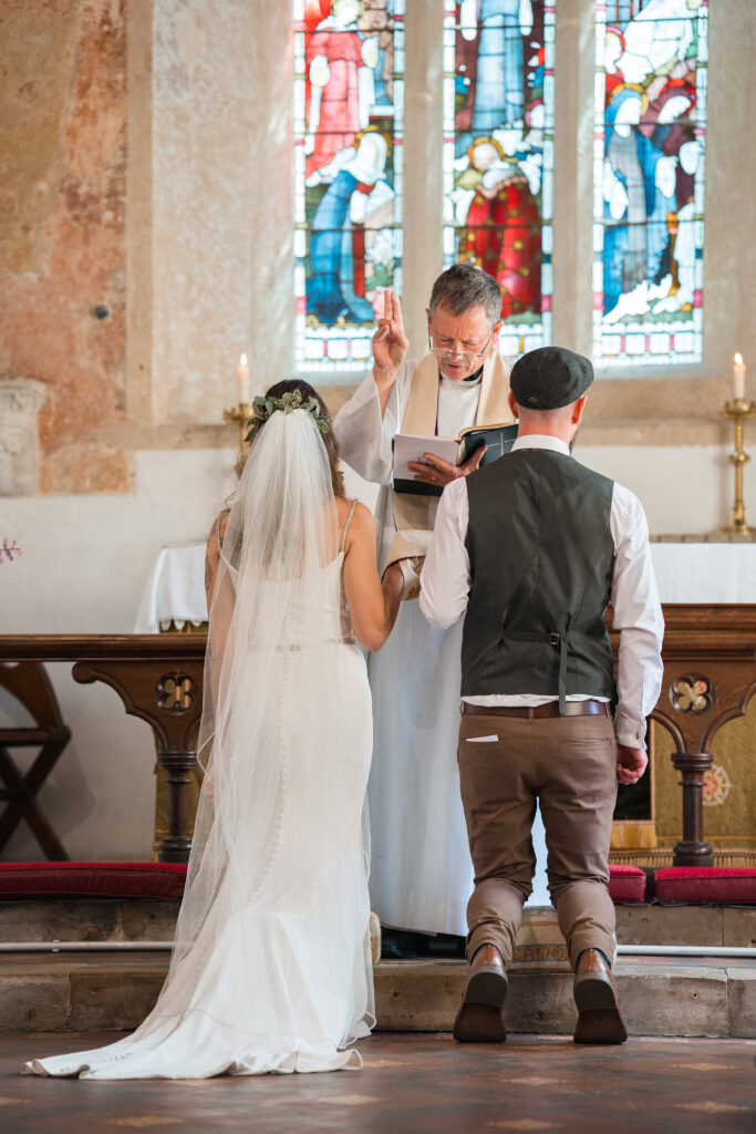 bride and groom kneel beneath stain glass window at new forest wedding